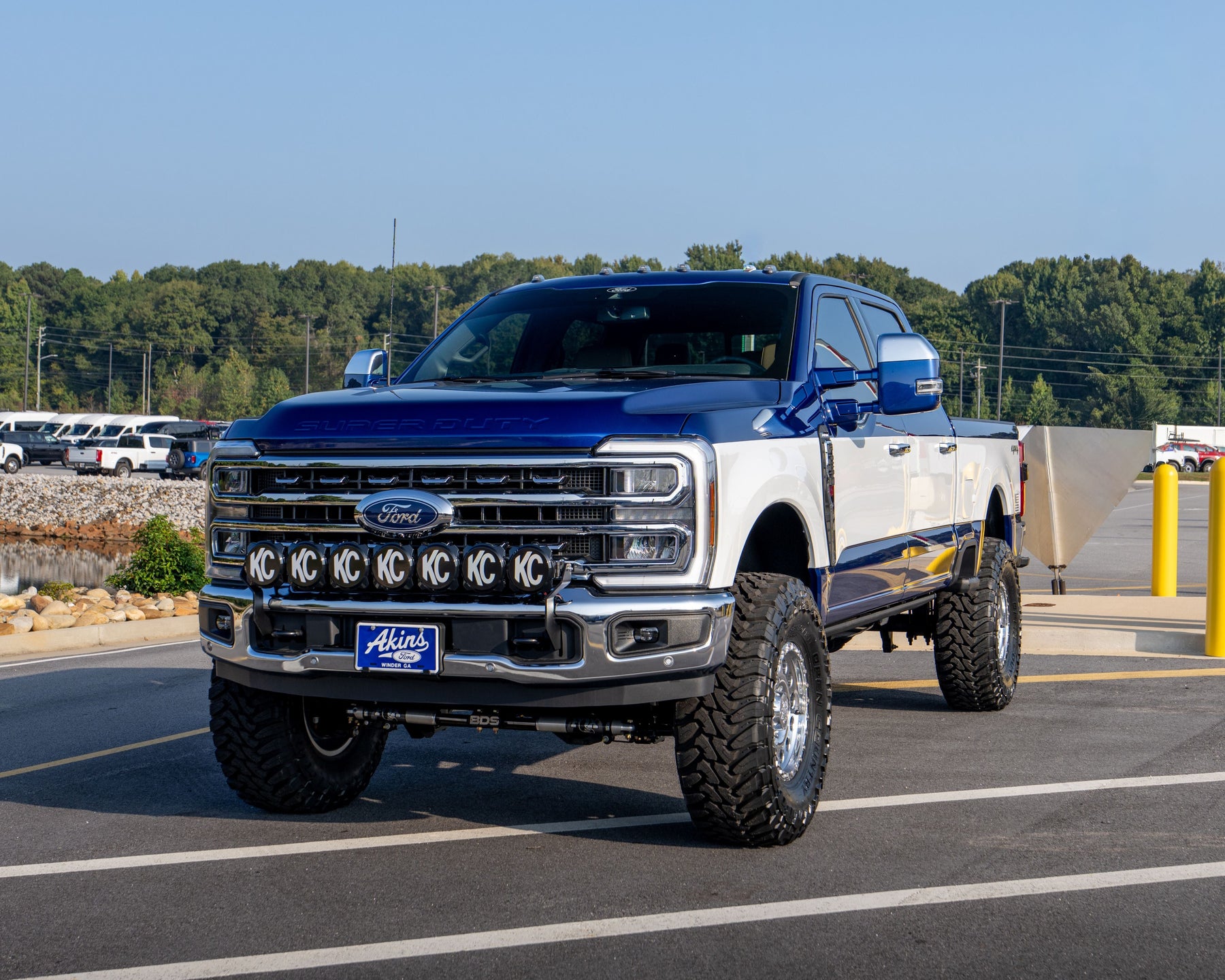 Wild Willies Custom Retro Tu Tone Ford Super Duty pickup truck with a blue and white paint job, featuring a chrome front grille, off-road tires, and a custom front bumper, parked on an outdoor paved road under a clear blue sky.